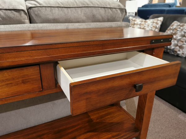 The Mango Sofa Table by Winners Only is styled traditionally with an open drawer against a gray sofa and patterned cushions.