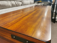 Close-up of the Winners Only Mango Sofa Table, crafted from polished wood with a metal bracket, sofa visible in the background.