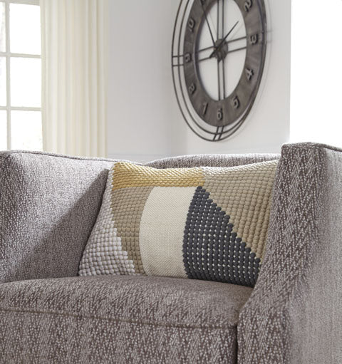 A gray upholstered armchair with the Ashley Shawn Pillow sits by modern art and a window with white curtains.