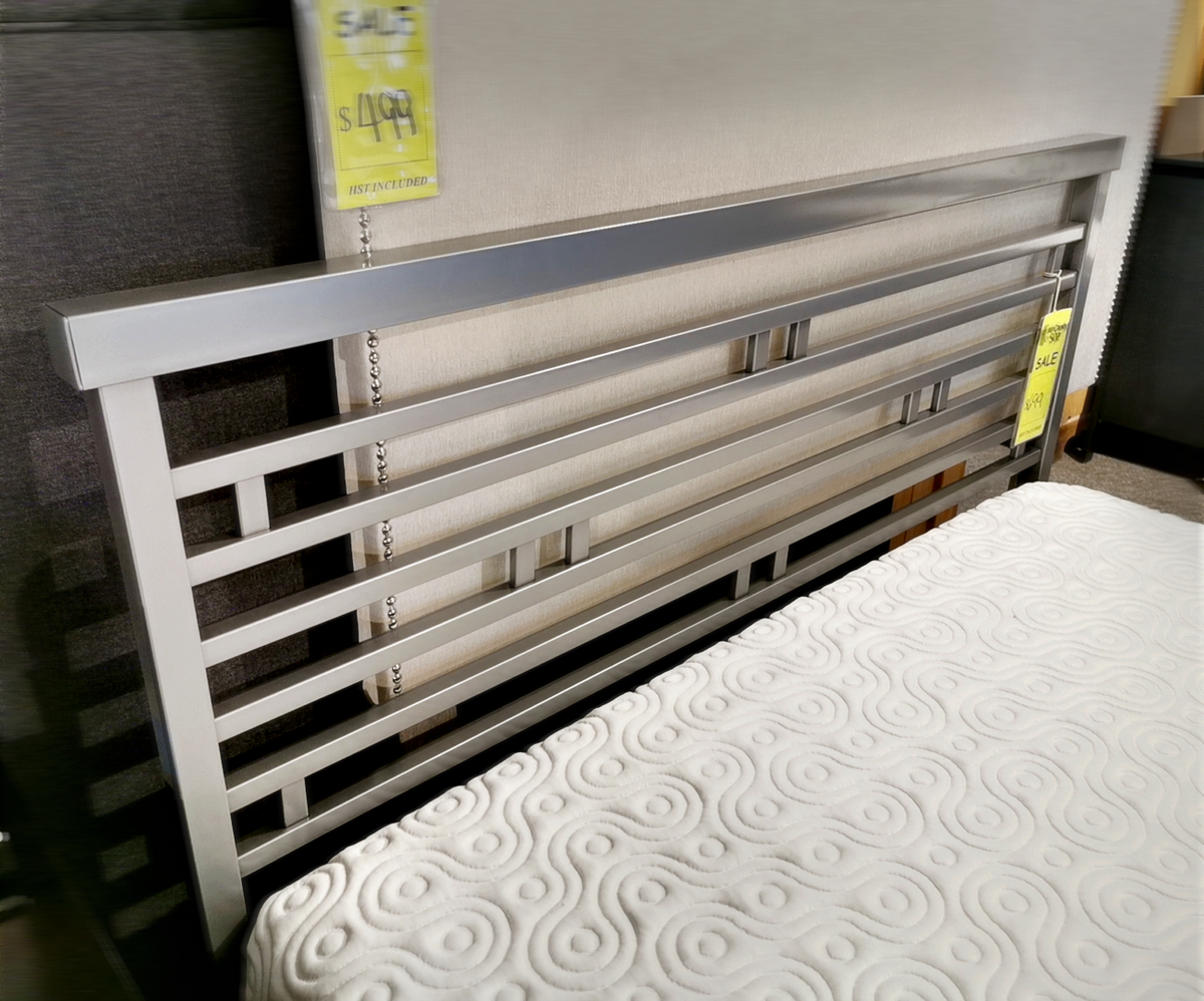 The Orson Bed Frame by Amisco, featuring a sleek metal structure with horizontal slats, is showcased in a store for $499.95. A white mattress adorned with a swirl pattern enhances the modern aesthetic at the front.