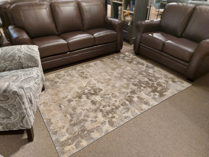 Brown leather couches and a patterned armchair surround the Ashley Jiro area rug in the living room.