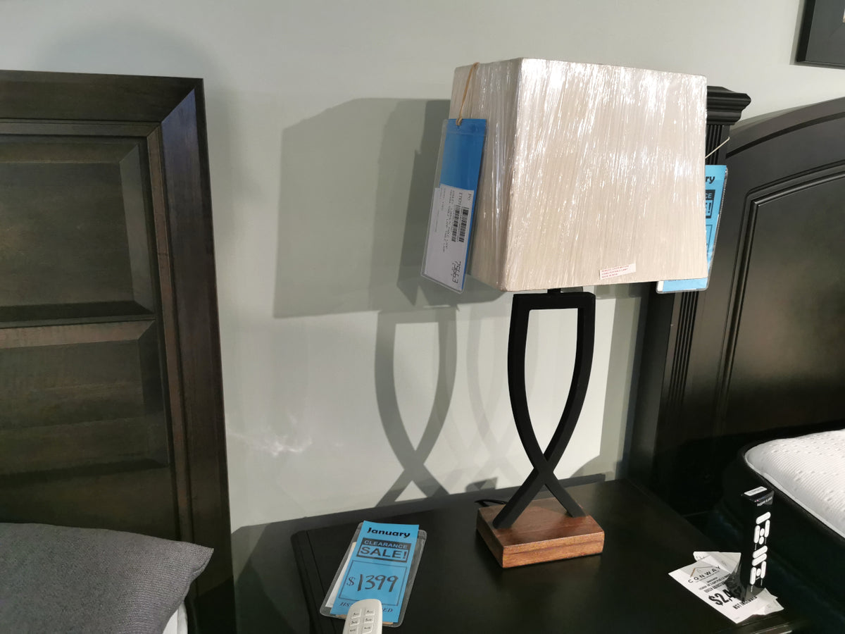 The Ashley L204174 Makara Table Lamp with a wood base is displayed between two dark wood bed frames.