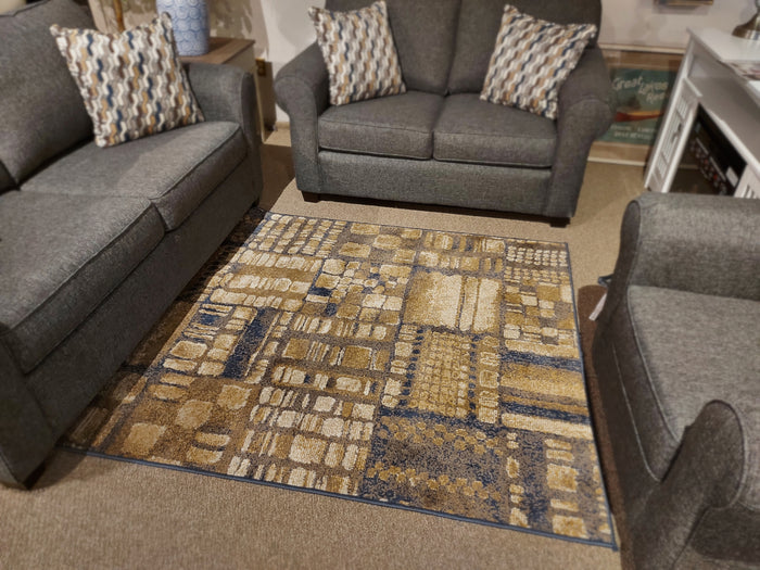 Contemporary gray living room set with the Ashley Hilliard area rug in beige, brown, and blue on carpeted flooring.