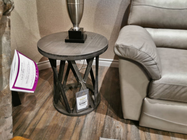 Ashley T711 Sharzane Round End Table, weathered wood with metal base, $289, next to a gray upholstered sofa.