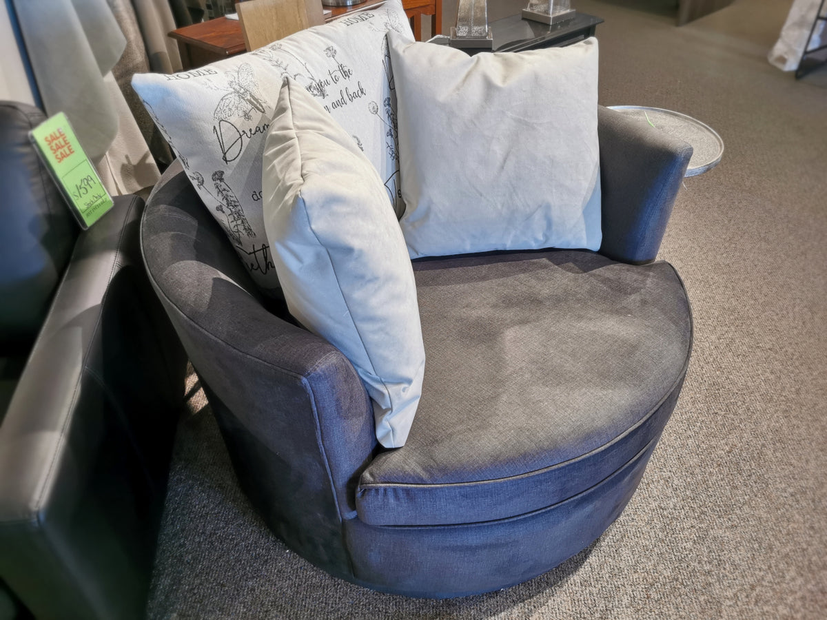 Round 46" Decor-rest 2991 Swivel Chair in gray, featuring two beige pillows and one print pillow, showcased on a carpeted floor. Custom order options are available.