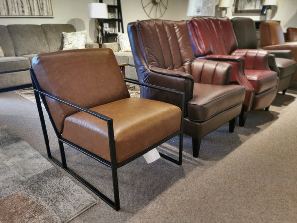 A row of five unique armchairs, featuring the Decor-rest 3071 Chair in brown leather, crimson leather, and tan leather designs, captures mid-century design flair and Hollywood glamour on a carpeted showroom floor.