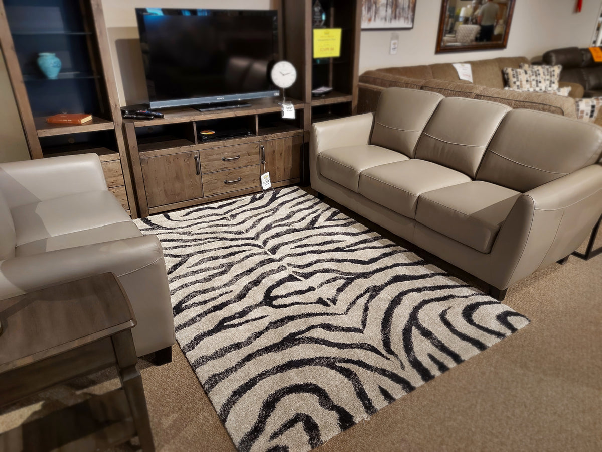 A living room display with a beige sofa set, wooden TV stand, and Kalora Sable 9652/P384 zebra pattern rug on carpet.