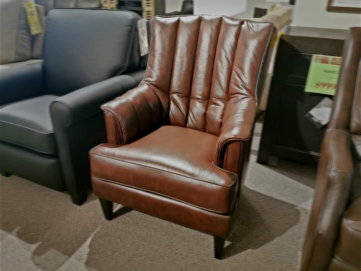 The 786 High Leg Chair by Leather Craft, a brown leather armchair with vertical stitching, displayed in a furniture showroom.