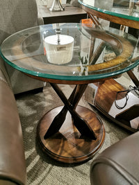 The T2214 Beaufort Round End Table by Magnussen is on a carpeted floor between brown leather chairs.