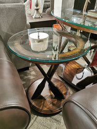 The T2214 Beaufort Round End Table by Magnussen sits between brown leather sofas in a showroom.