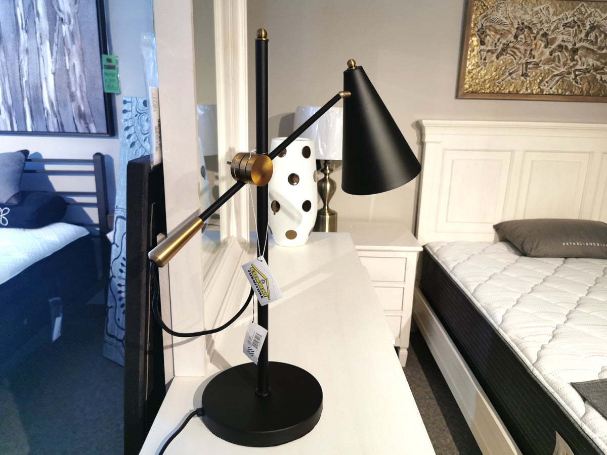 The Mercana 65226 Fragon 2 Desk Lamp in matte black and gold sits on a white dresser in a styled bedroom.