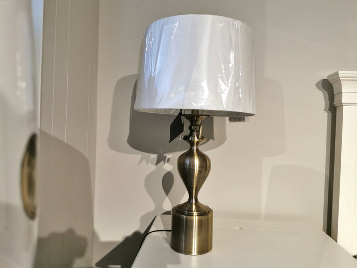 The Pacific Coast 87-7773-02 Brazza Table Lamp with a linen shade sits on a white surface by a beige wall.