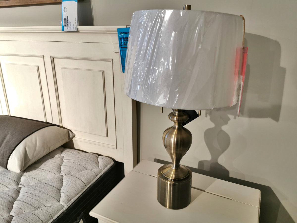The Pacific Coast 87-7773-02 Brazza Table Lamp with a linen shade sits on a nightstand by a white headboard.