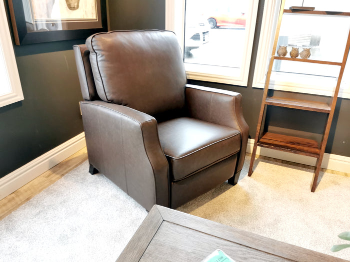 A Superstyle L86 Leather Power Recliner sits on a light carpet by a window and wooden shelf in a well-lit room.