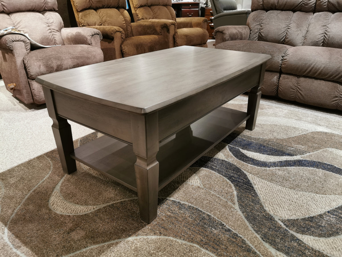 The Annapolis 48" Coffee Table by Winners Only, featuring solid hardwood construction and a lower shelf in gray wood, is placed on a patterned carpet and surrounded by brown recliner chairs.