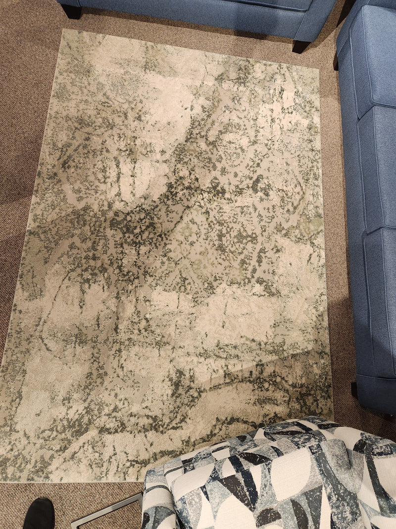 The Rizzy Home Chelsea 5'3" x 7'6" Area Rug in beige and green pairs well with blue, patterned furniture on carpeted floors.