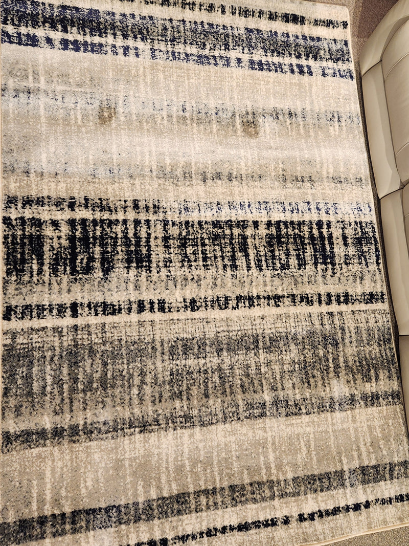 The Kalora Abbey 33005/160 5'1" x 7'7" area rug with blue, gray & beige stripes pairs well with a beige couch.