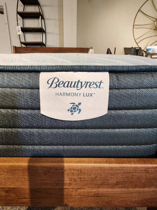 Close-up of a Beauty-rest Guava Gulf TT Firm Mattress in a showroom, showcasing the brand label and part of a wooden bed frame, promising firm support for restorative sleep.