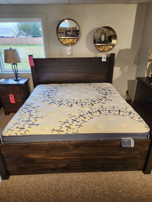 Bedroom setup with wooden bed, Stearns & Foster mattress, two round mirrors, lamp, and nightstand on display.