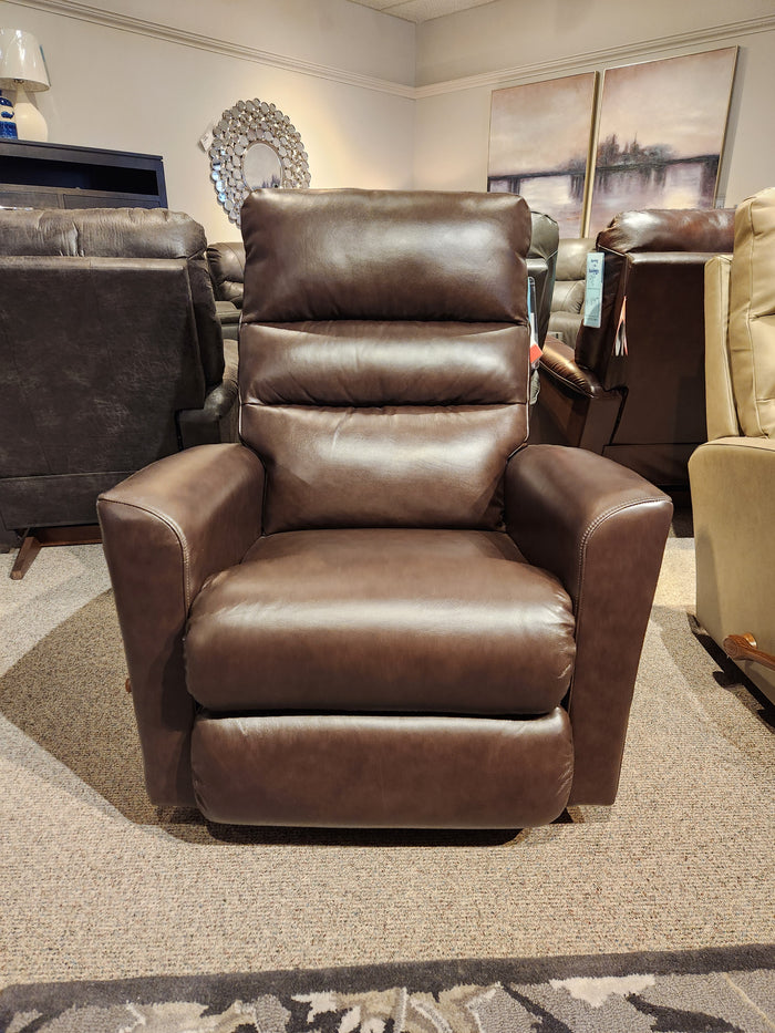 The 786 Liam Rocker Recliner from La-z-boy, featuring a casual style, is displayed in a showroom. Surrounded by other furniture pieces, this brown leather recliner offers comfort and relaxation for any living space.