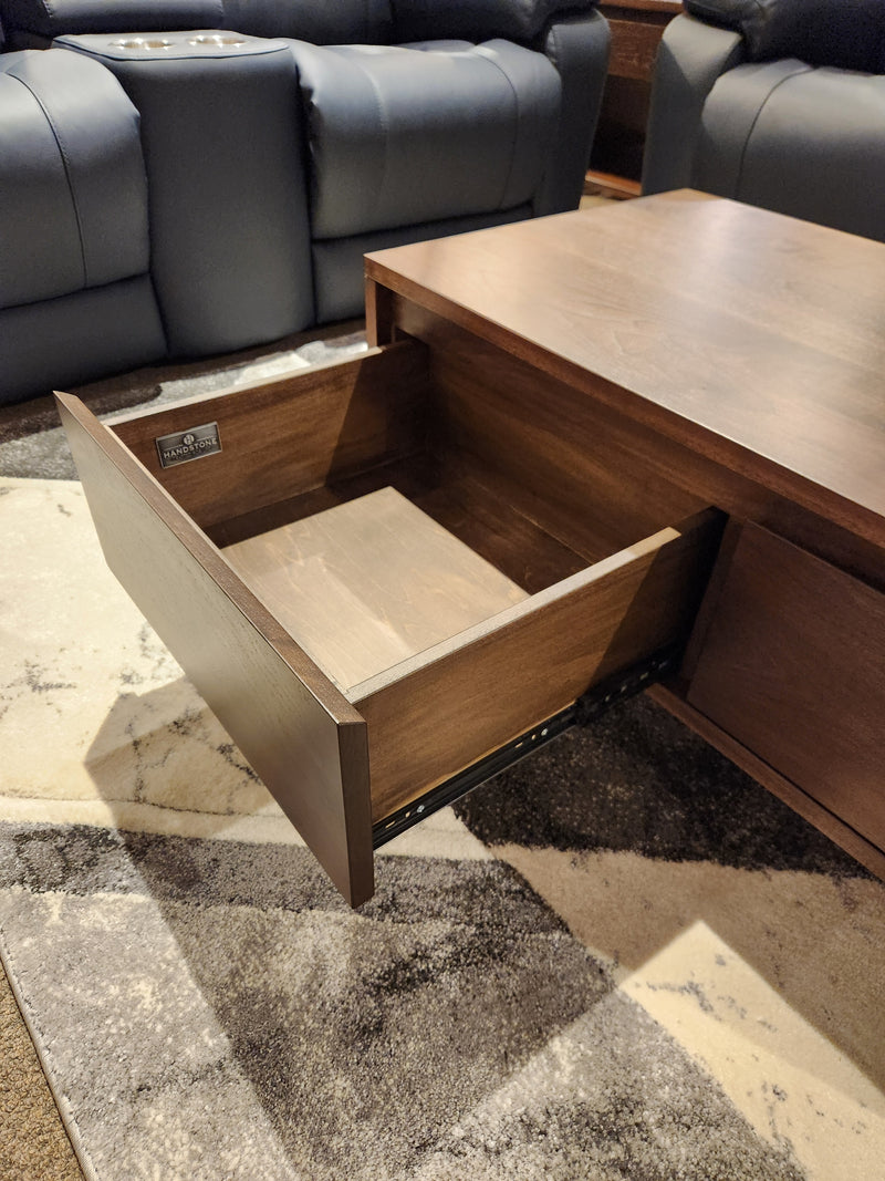 The Handstone N-EV2140 Evora Condo Coffee Table with open drawer sits on a rug near dark chairs.