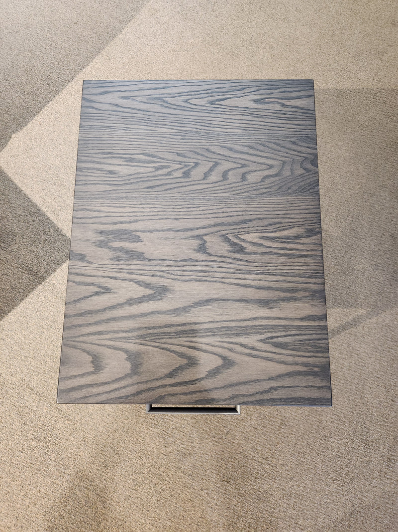 The Muskoka 18" End Table by Handstone features a solid oak top and gray wood grain, standing on a light carpeted floor.