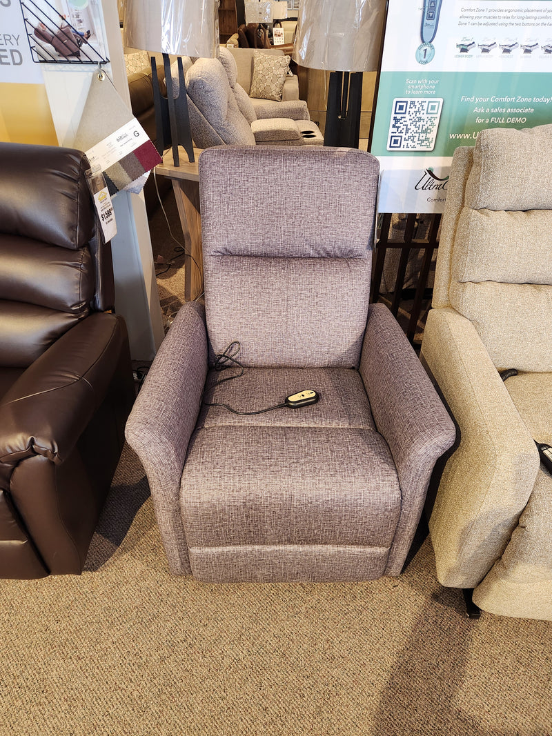 The gray Primo Thorley Power Lift Chair offers comfort and reliability, featuring an attached remote on a carpeted showroom floor.