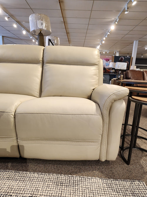 A beige leather Cascade Power Sofa by Aurora Furniture, with a power headrest, displayed under showroom lighting.