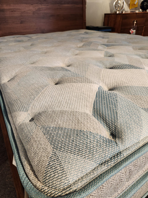 Close-up of a Beauty-rest Keegan Pillow-Top Plush mattress on a wooden bed frame in a showroom.