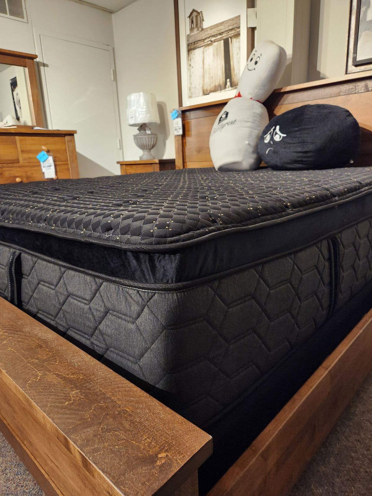 A Beauty-rest Hermes Ultra Plush Mattress in black with a hexagonal pattern sits on a wooden frame, styled with decor.