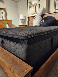 A Beauty-rest Hermes Ultra Plush Mattress in black with a hexagonal pattern sits on a wooden frame, styled with decor.