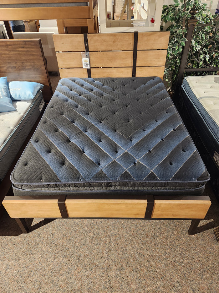 A Beauty-rest Lusso Plush SPT Mattress by Beauty-rest on a wooden bed frame displayed in a showroom.