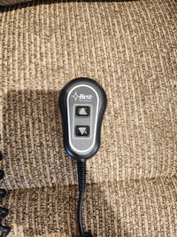 A black wired remote for the Best 7MP84 Ellisport Power Space Saver Recliner sits on a brown textured fabric.