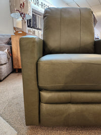 Green leather Kristisha Swivel Push-back Recliner by Best, with modern silhouette, displayed on carpeted store floor.