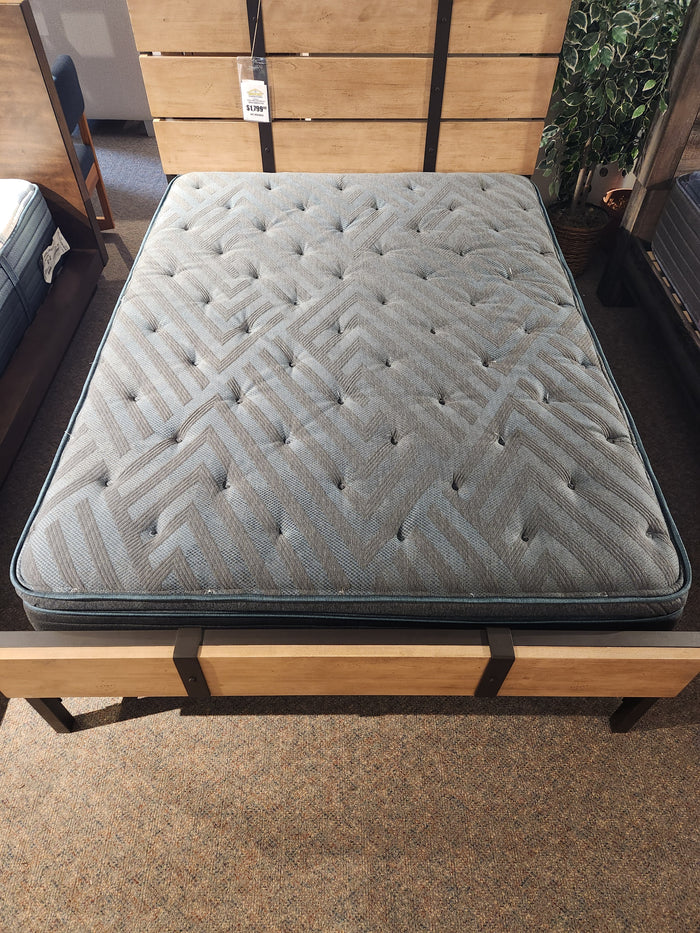 The Beauty-rest Eryx PT Medium Mattress in gray with a geometric pattern sits on a wooden frame in a stylish showroom.
