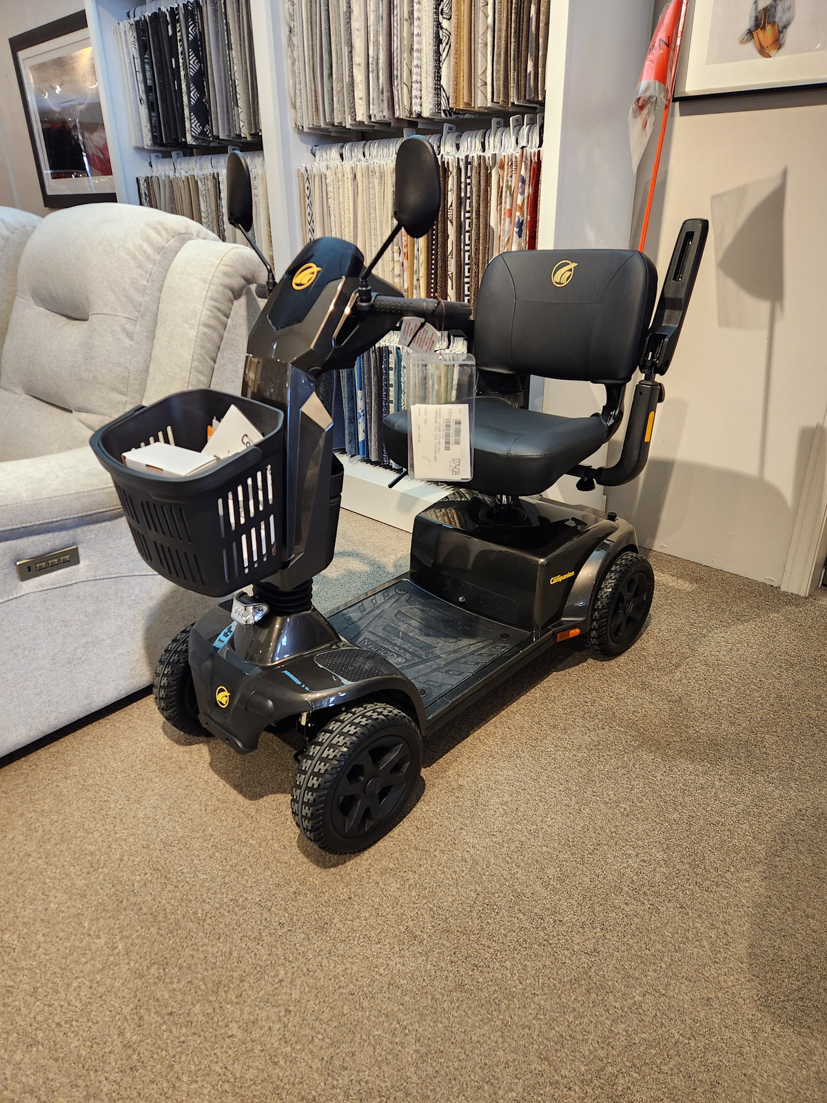The Golden Companion Full-Size Mobility Scooter, black with 4 wheels and a front basket, is shown indoors on carpet.
