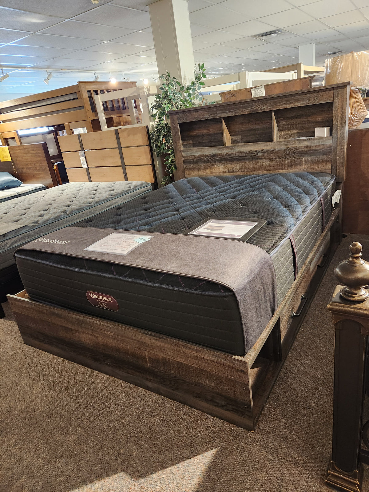 A queen bed with storage, headboard shelf, and Beauty-rest ESME TT Medium Mattress is on display in the showroom.