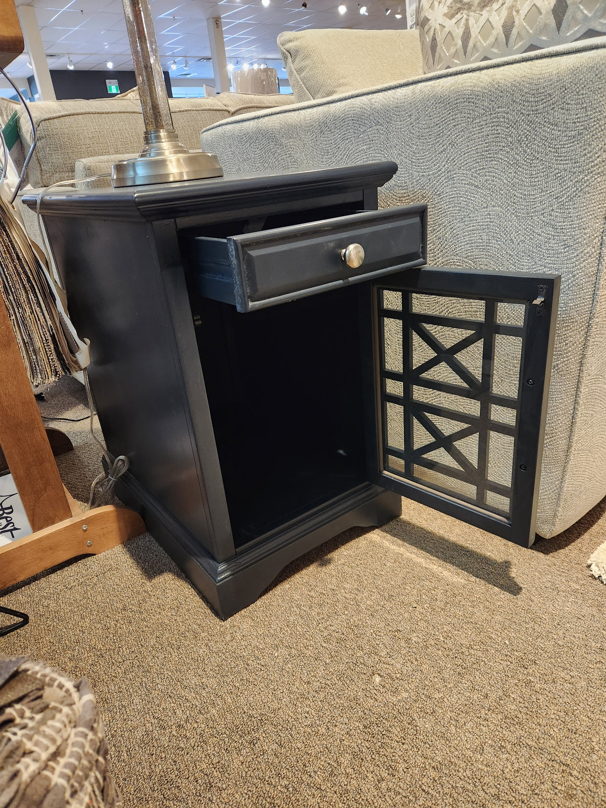 A Jofran Craftsman Power Chairside Table in black with antique hardware, drawer, and open cabinet sits by the sofa.