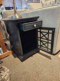 A Jofran Craftsman Power Chairside Table in black with antique hardware, drawer, and open cabinet sits by the sofa.