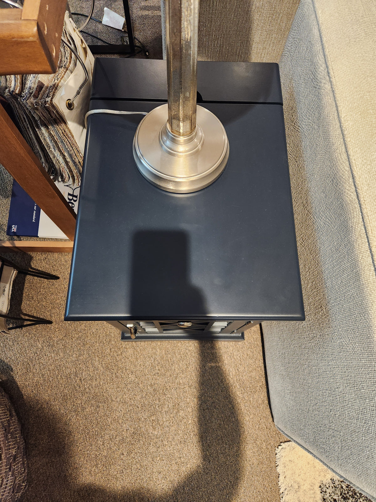 A lamp with a metallic base adds timeless charm atop the Jofran Craftsman Power Chairside Table beside a sofa.