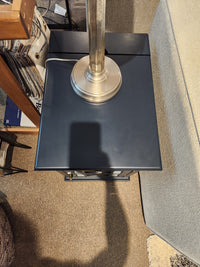 A lamp with a metallic base adds timeless charm atop the Jofran Craftsman Power Chairside Table beside a sofa.