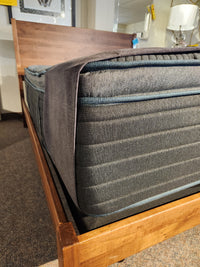 Close-up of a Beauty-rest Echo PT Medium Mattress with gray fitted sheet on wood bed frame in a showroom.