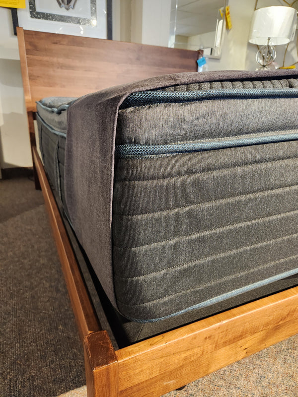 Close-up of a Beauty-rest Echo PT Medium Mattress with gray fitted sheet on wood bed frame in a showroom.