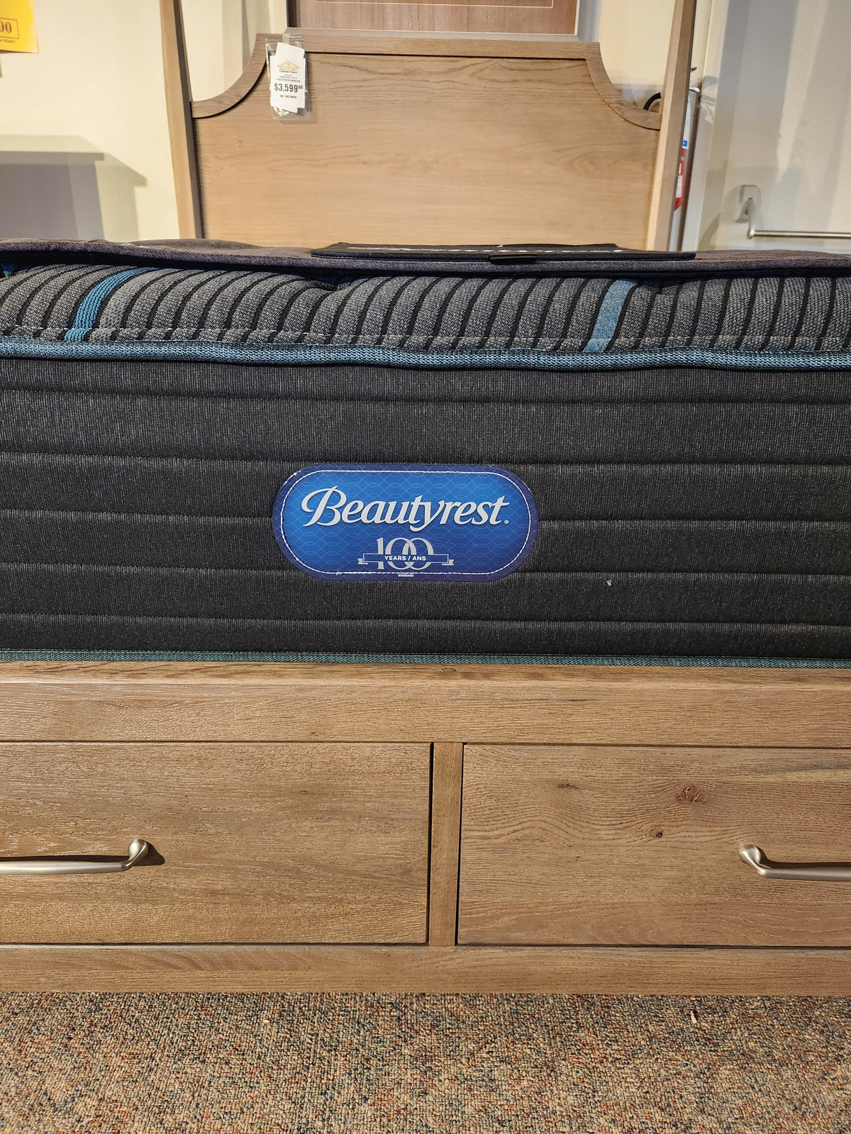 A Beauty-rest Mira TT Medium Mattress rests on a wooden drawer platform in the showroom.