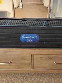 A Beauty-rest Mira TT Medium Mattress rests on a wooden drawer platform in the showroom.
