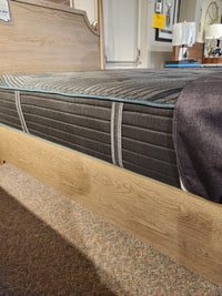 A close-up of the Beauty-rest Mira TT Medium Mattress by Beauty-rest on a wooden bed frame in a carpeted showroom.