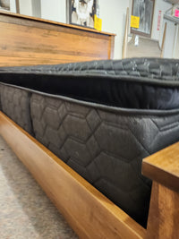 A close-up of the Beauty-rest Adonis PT Plush Mattress on a wooden bed frame in a showroom.