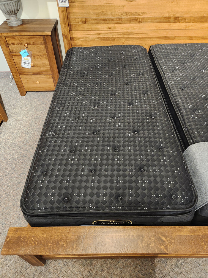A black Beauty-rest Adonis PT Plush twin mattress rests on a wood bed frame beside a matching nightstand.
