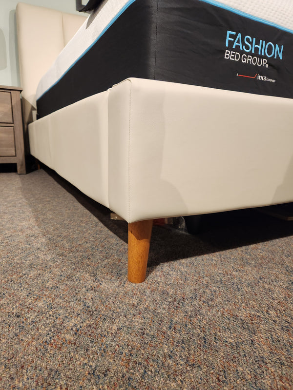 Close-up of a Palliser 77140 Verttia King Upholstered Bed corner with a wooden leg on a carpeted floor.