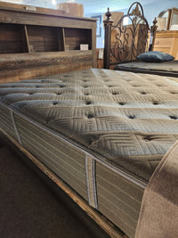 A close-up of a Beauty-rest Haven TT Firm Mattress by Beauty-rest on a wooden bed frame in a showroom.